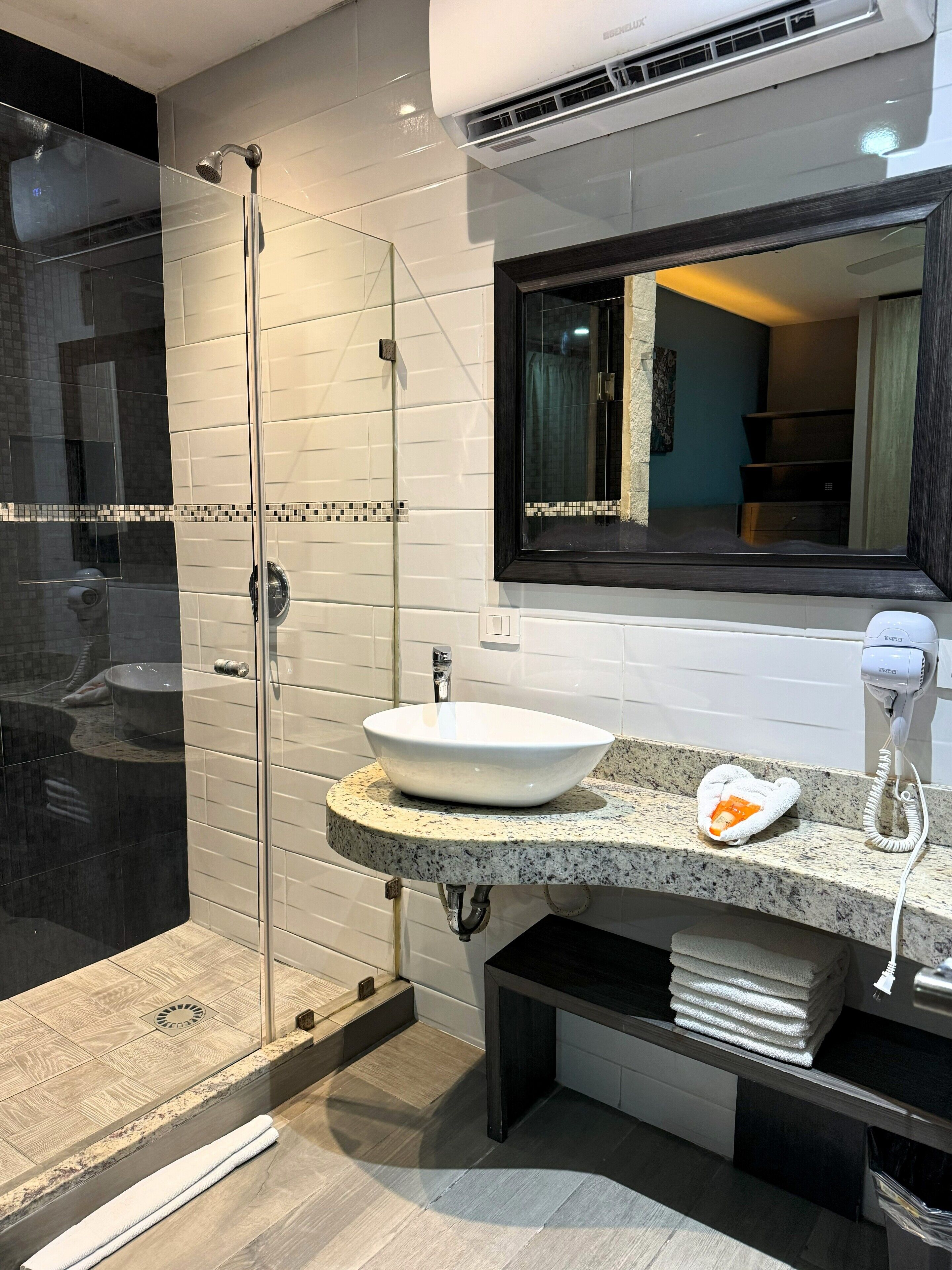 Un baño moderno con ducha de vidrio, un lavamanos blanco y un secador de pelo sobre la encimera.
