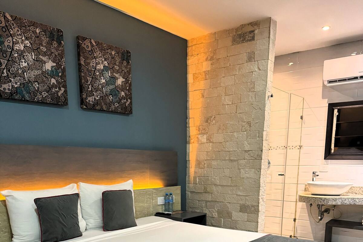 A hotel room with a large bed, a stone accent wall, a modern bathroom, and artwork on the wall.