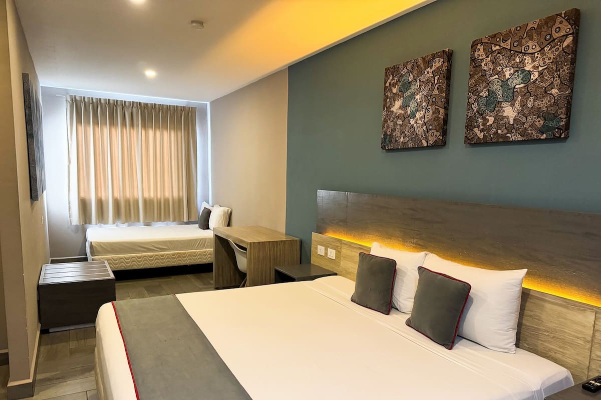 A hotel room with a large bed, a desk, a chair, and two paintings on the wall.