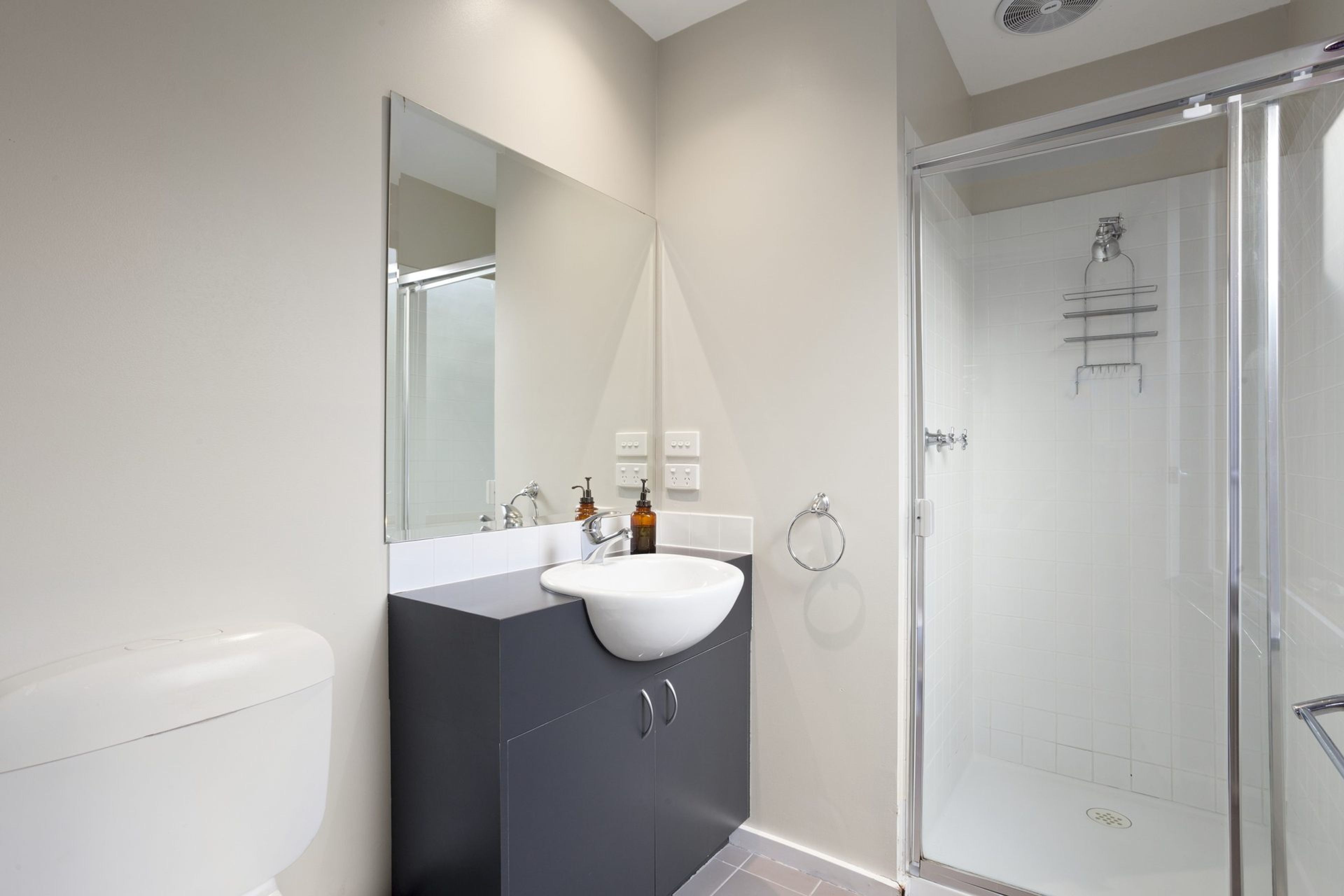 A modern bathroom with a glass shower enclosure, a white sink, and a dark vanity.