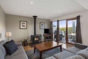 A spacious living room with a fireplace, a television, and a balcony with outdoor furniture. - Otway Vista 12 (Apollo Bay)