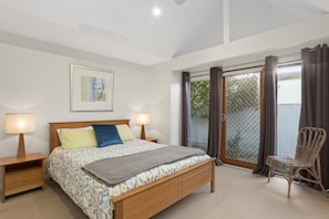 A bedroom with a bed, two bedside tables, a chair, a window with curtains, and a ceiling fan. - Otway Vista 12 (Apollo Bay)