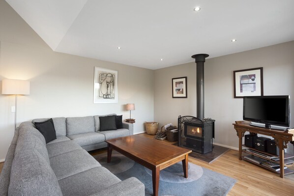 A modern living room with a sectional sofa, a wooden coffee table, a fireplace, a television, and artwork on the walls. - Otway Vista 12 (Apollo Bay)