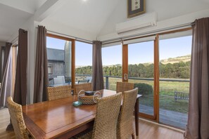 A dining area with a wooden table and wicker chairs, large windows with curtains, and an air conditioning unit on the ceiling. - Otway Vista 12 (Apollo Bay)