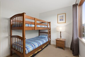 A bunk bed with a matching headboard, a bedside table with a lamp, a framed picture on the wall, and a window with curtains. - Otway Vista 12 (Apollo Bay)