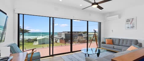 A spacious living area with a large sliding glass door leading to a balcony overlooking the ocean.