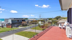 A balcony with a red floor, overlooking a residential area with houses, a road, and a beach. - Casino Views (Apollo Bay)