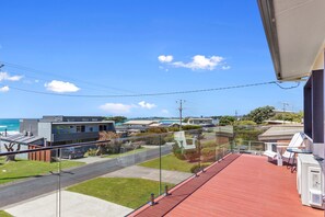 A balcony with a red floor, overlooking a residential area with houses, a road, and a beach. - Casino Views (Apollo Bay)