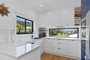 A modern kitchen with white cabinetry, a large window, and a built-in oven. - Casino Views (Apollo Bay)