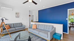 A modern living room with a ceiling fan, a sofa, a coffee table, and a small blue ottoman. - Casino Views (Apollo Bay)