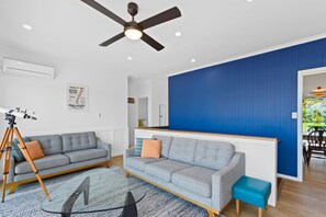 A modern living room with a ceiling fan, a sofa, a coffee table, and a small blue ottoman. - Casino Views (Apollo Bay)