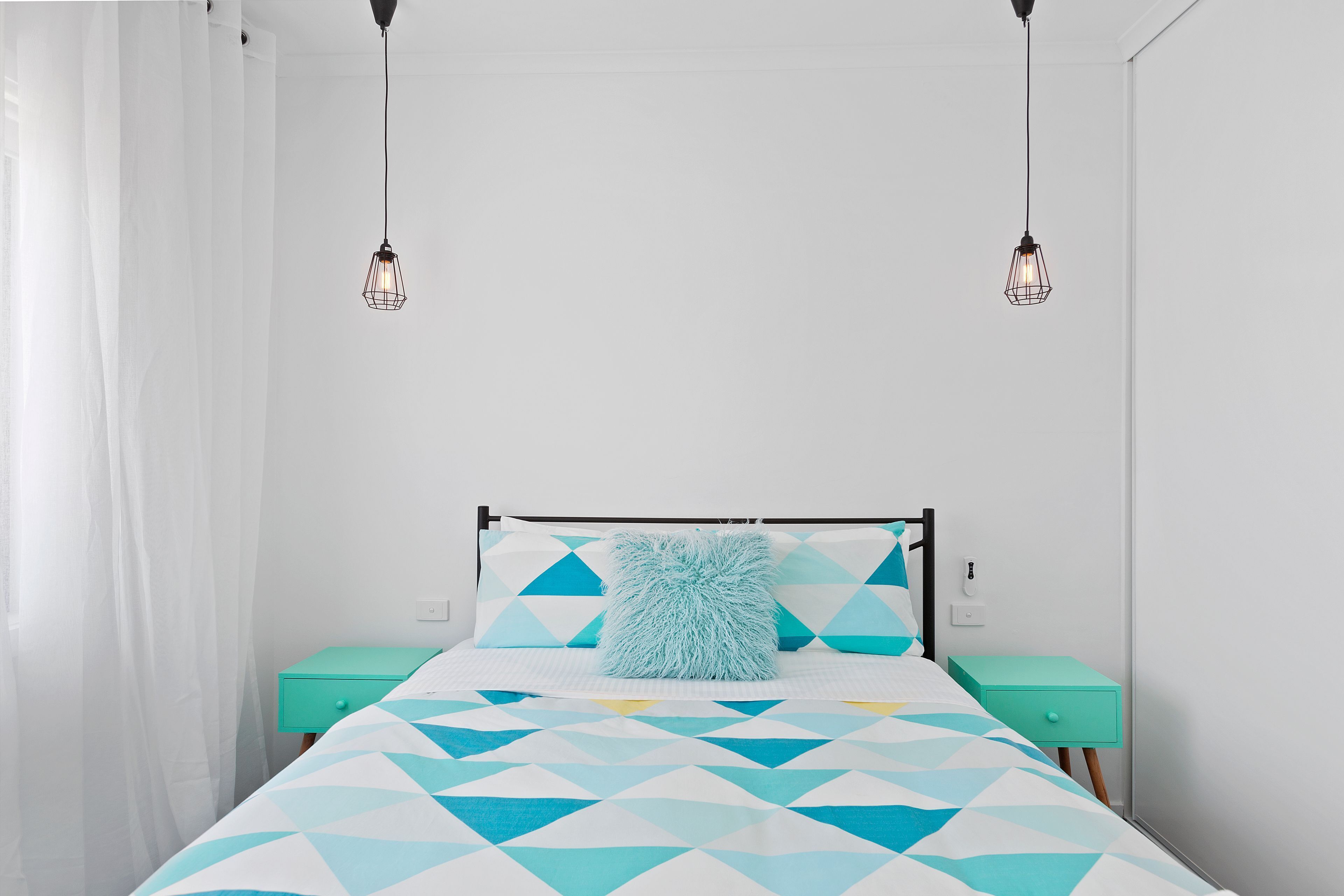 A bed with a geometric patterned bedspread, two bedside tables, and a hanging light fixture.
