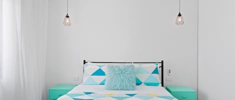 Ein Bett mit einem geometrisch gemusterten Überwurf, zwei Nachttische und eine hängende Deckenleuchte.
