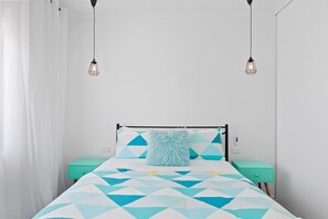 Una cama con colcha de estampado geométrico, dos mesitas de noche y una lámpara colgante.