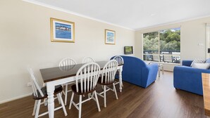 A dining area with a wooden table and white chairs, a blue sofa, and two framed pictures on the wall. - Summer Breeze (Apollo Bay)