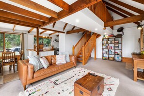 Un amplio salón con una escalera de madera, un sofá de cuero y una estantería.