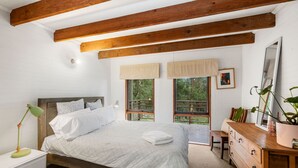 Una camera da letto con un letto, un comodino, una cassettiera e una finestra vista verde.