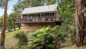Una casa in legno a due piani con un balcone, immersa nel verde e circondata da alberi.