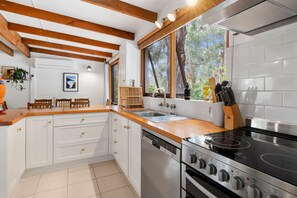 A kitchen with white cabinetry, a wooden countertop, a stove, and a window with a view of trees.