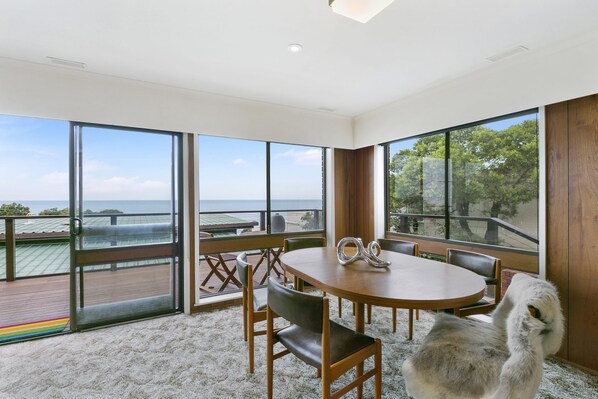 A spacious room with a large table and chairs, large windows with a view of the sea, and a balcony with a railing. - 1 at Fifty Nine Beach Classic in Lorne (Lorne)
