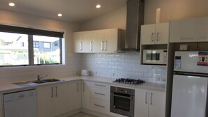 A modern kitchen with white cabinets, a built-in oven, a microwave, and a dishwasher. - stunning 2 bedroom 2 bathroom holiday home with a kiwiana caravan for extra beds (Ohope)