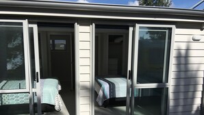 A room with two beds, a sliding glass door, and a window with blinds. - stunning 2 bedroom 2 bathroom holiday home with a kiwiana caravan for extra beds (Ohope)