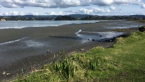 A coastal landscape with a wide sandy beach, grassy areas, and a calm body of water. - stunning 2 bedroom 2 bathroom holiday home with a kiwiana caravan for extra beds (Ohope)