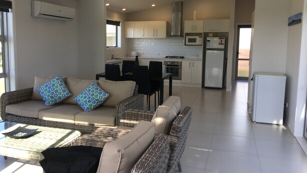 A modern living room with a sofa, chairs, and a coffee table. There is a kitchen area with cabinets, a refrigerator, and a microwave. - stunning 2 bedroom 2 bathroom holiday home with a kiwiana caravan for extra beds (Ohope)