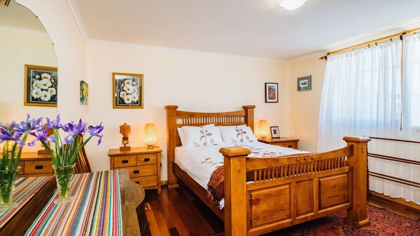 A bedroom with a wooden bed, bedside tables, a striped tablecloth, and a vase of purple flowers. - The blue beach house (Quinns Rocks)