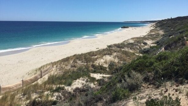 A beach with a sandy shore and a grassy hill in the foreground. - The blue beach house (Quinns Rocks)