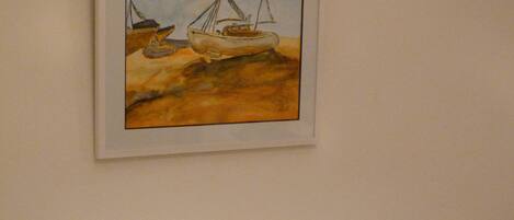 A framed artwork of a boat on a rocky shore.