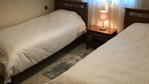 A bedroom with two single beds, a bedside table with a lamp, a wall-mounted air conditioner, and a window with sheer curtains. - Résidence Les Ambassadeurs (Rabat)