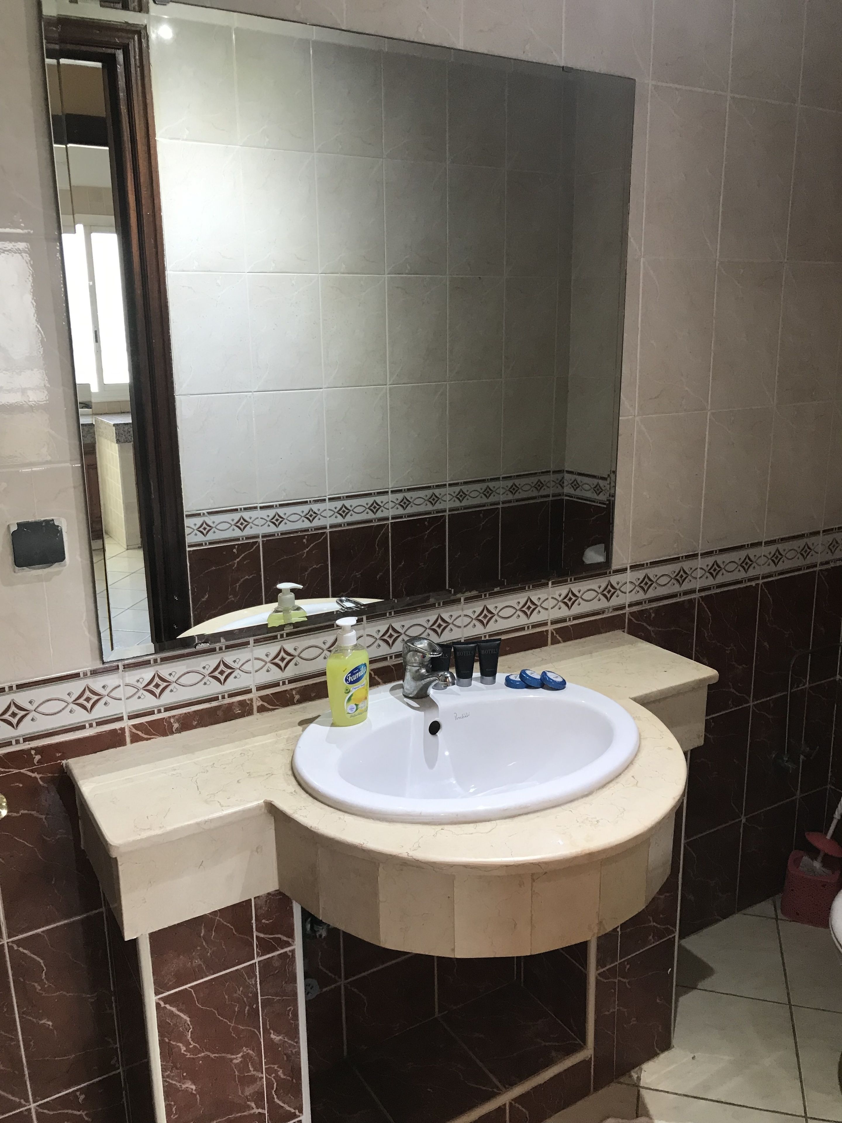 Un baño con lavamanos blanco, un espejo y un inodoro. Hay artículos de tocador en la encimera del lavamanos.
