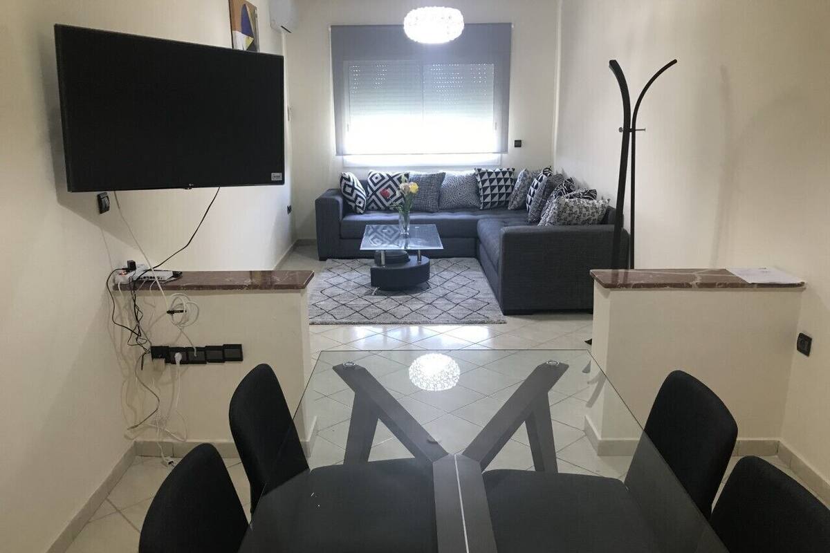 A modern living room with a sofa set, a glass coffee table, and a TV mounted on the wall.