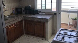 A kitchen with wooden cabinets, a gas stove, a microwave, and a window overlooking a balcony. - Résidence Les Ambassadeurs (Rabat)