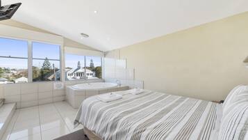 A modern bedroom with a large bed, a bathtub, and a view of a residential area.