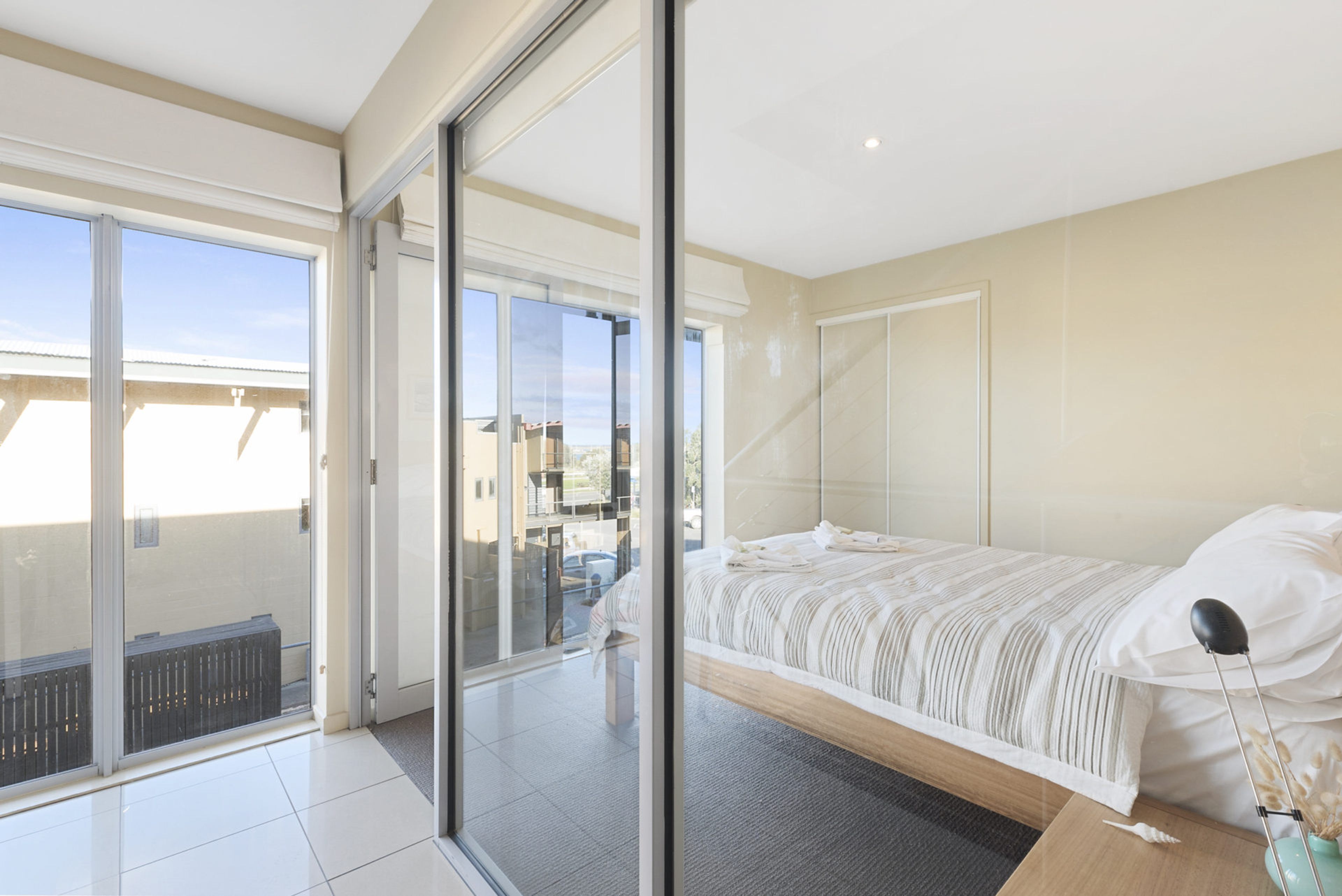 Une chambre à coucher avec un lit, une table de chevet, une lampe et une vue sur l’extérieur, accessible par une porte-fenêtre coulissante.