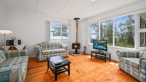 A cozy living room with a fireplace, two patterned sofas, a coffee table, and a television. - On Collingwood Beach  by Book Jervis Bay - Upstairs Apartment (Vincentia)
