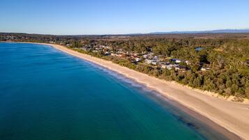 An aerial view of Collingwood Beach with a clear blue sea, sandy beach, and residential area with houses.