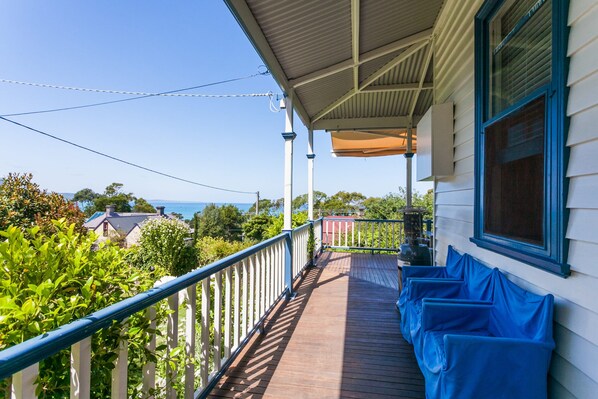 A wooden deck with a railing, a covered area with a window, and a view of the sea and houses in the background.
