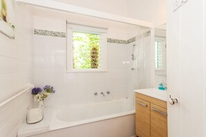 A bathroom with a bathtub, a window with a view of greenery, and a vanity with a mirror. - Valetta (Lorne)