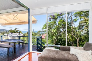 Ein Balkon mit Tisch und Stühlen, einer Couch und Blick auf Grünflächen und eine entfernte Landschaft.