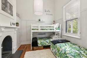 Ein Kinderzimmer mit Etagenbetten, Kamin und einem Fenster mit Jalousien.
