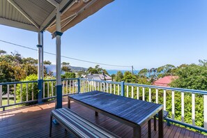 A wooden deck with a table and bench, overlooking a residential area with houses and trees.