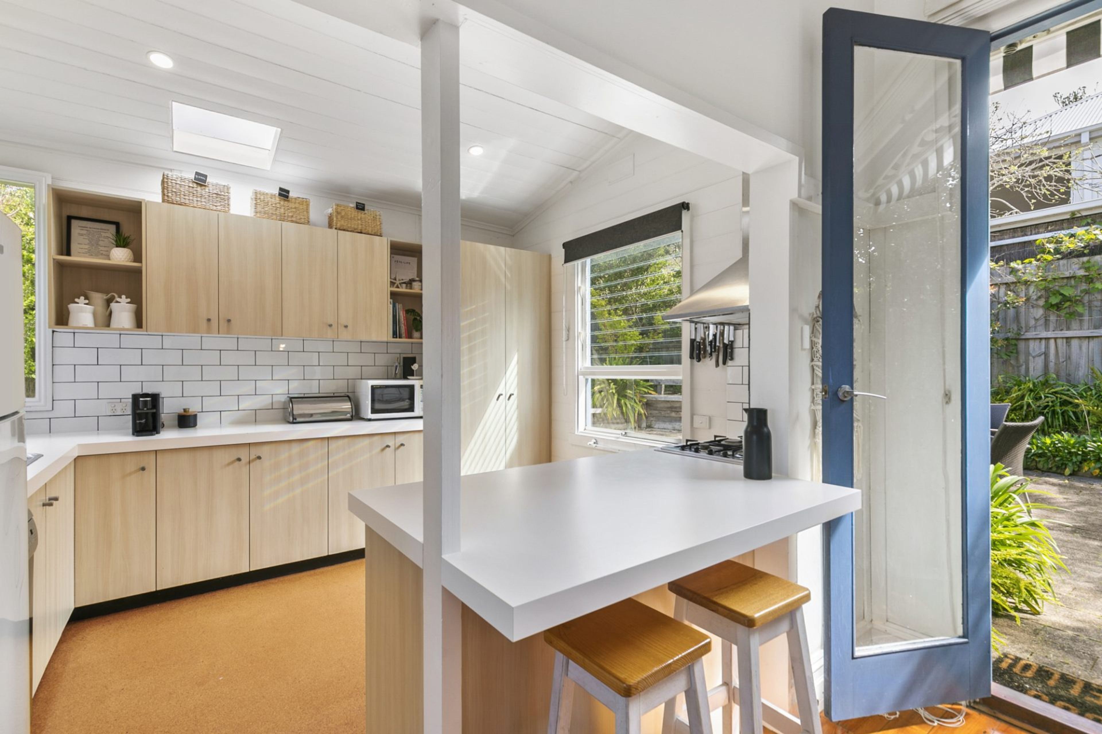A compact kitchen with a white countertop, wooden cabinets, and a view of the garden through a glass door.