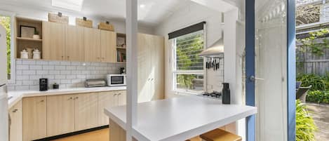 A compact kitchen with a white countertop, wooden cabinets, and a view of the garden through a glass door.