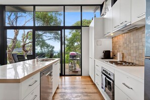 Une cuisine moderne dotée d’un grand îlot central, de meubles blancs et offrant une vue sur l’extérieur.