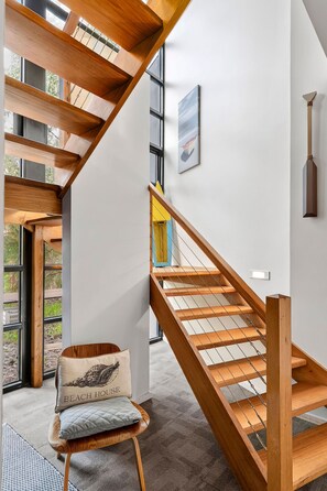 Un interno moderno con una scala in legno, una sedia con cuscino e un quadro appeso al muro.