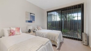 Two single beds with white duvets and decorative pillows, surrounded by a minimalist design and a large sliding door leading to an outdoor area with a view.