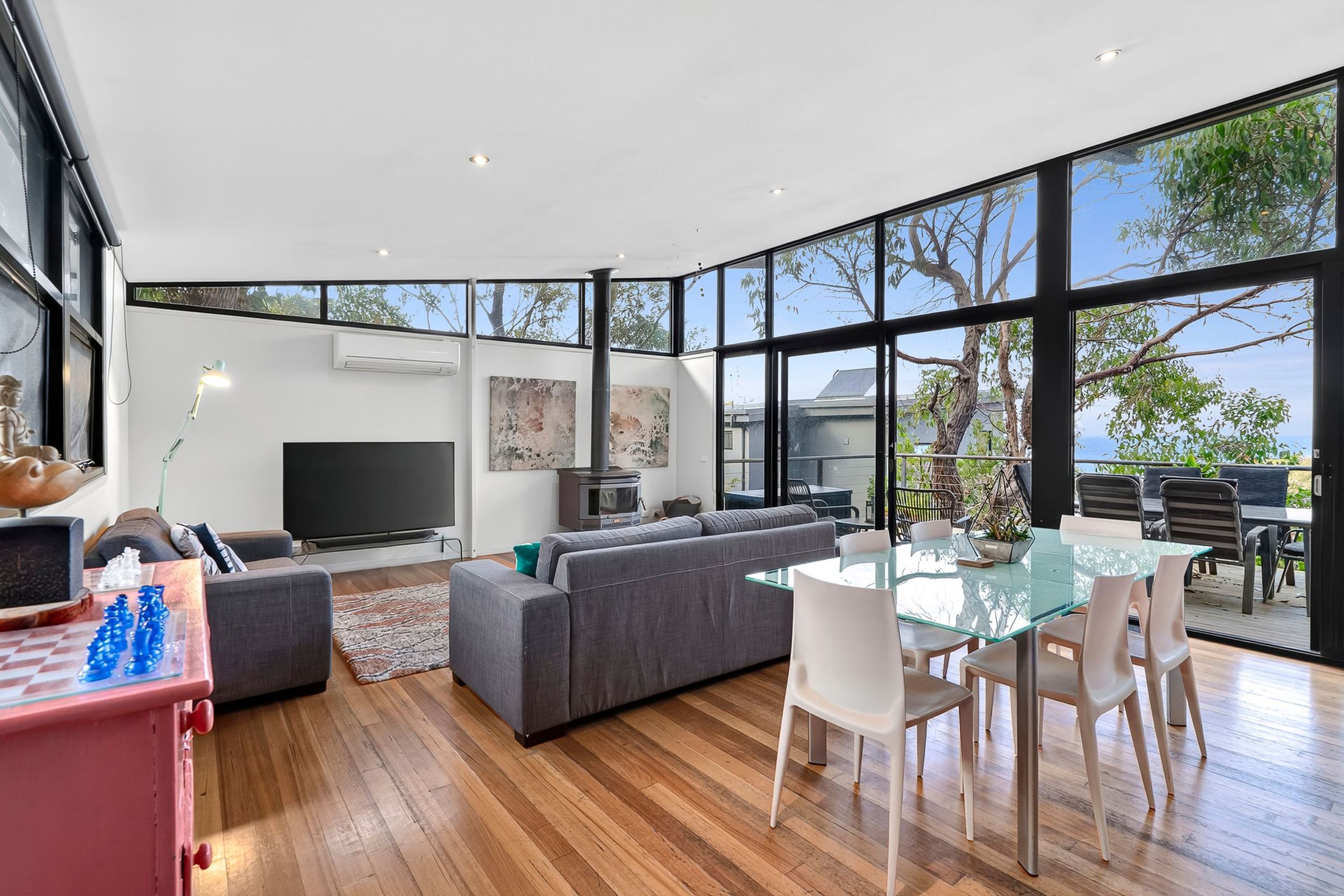 A modern living room with a large window, a flat-screen TV, a sofa, and a dining area with a glass table.